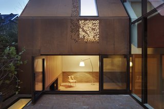 Weathered Steel Clads a $4.7M Home Near London’s Kew Gardens - Photo 2 of 10 - Brick and oak line the interior of the living room, where a wood-burning stove creates a welcoming ambiance. A large picture window opens onto the courtyard. Above, a perforated steel panel allows for an interplay of light and shadow. 