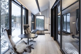 Go Stargazing in Snøhetta’s Towering Addition to Sweden’s Treehotel - Photo 3 of 7 - Light ash flooring and birch plywood walls create a light interior that contrasts the dark, charred exterior wood. Here in the lounge space, simple furniture such as the Scandia Chair by Hans Brattrud and a central pellet stove create a calm, inviting environment. A floor-to-ceiling window, facing north, is your best bet for seeing the Aurora Borealis. 