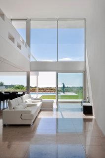 The open kitchen, dining, and living area boasts high ceilings above and natural stone tiles below. Sliding glass doors lead to the outdoor patio and heated pool.