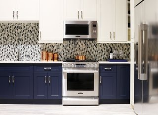 Signature Kitchen Suite’s Modern Pavilion Shines at KBIS - Photo 5 of 7 - The Signature Kitchen Suite Smart Kitchen is outfitted with navy and ivory cabinets by Green Forest Cabinetry and a glass tile mosaic backsplash. For Fuller, who comes from a product design background, the "smart thinking" of the brand's designs put them ahead of the curve. For example, the Gas Slide-In Oven Range above has an Easy Swivel Handle that is easier and safer to operate, and the capacious refrigerator benefits from a SmartSpace System ice dispenser that maximizes storage space.