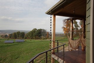 Located outside of State College, Pennsylvania, the home enjoys rolling green vistas. Two hammocks on the porch are ideal places to take in the views or a good book. The solar array, pictured in the midground, powers the home.