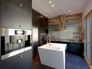 The kitchen boasts Forest Stewardship Council-certified bamboo cabinets and stainless steel and concrete countertops. The appliances are by Miele, Leibherr, and GE. Bi-fold glass doors connect the space to the outdoor dining area. 
