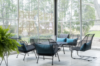 A Rare Midcentury Prefab Looks Just Like it Did in 1958—Down to the Knoll and Paul McCobb Interiors - Photo 8 of 13 - The aviary is Valentine's favorite room in the house. Located off the dining room, it has floor-to-ceiling Plexiglass panels that can be interchanged with screens in the fall. (Dr. Frost had fastidiously labeled every movable element in the residence to ensure that everything would be returned to the exact same place.) West Elm Iris Planters add extra greenery beside Russell Woodard Sculptura patio furniture, topped with Restoration Hardware pillows.