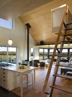 Sliding fabric panels allow the enclosed porch to be used for dining or overflow sleeping. A loft overlooking the main living space and views of the farm serves as office space.