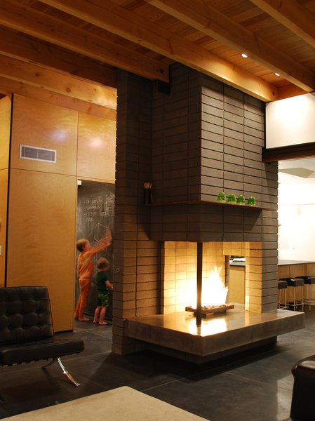 A new multi-functional space, and a remodeled kitchen and dining room, all revolve around a new three-sided fireplace. The fireplace is at the nucleus of the space and acts as a focal point while separating the spaces. The fireplace is positioned to open to all of the living spaces as well as the exterior patio. Photo 7 of The Silvertree Residence modern home