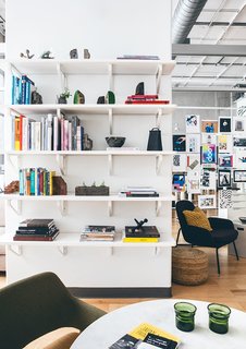 Open shelving and books with a sea of posters in the rear brings color and life to the sea of whites, grays, and light wood flooring.