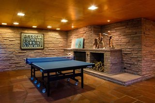 What Would Victor Do? - Photo 4 of 11 - The rumpus room delighted the Kohn<br>family, with its sprawling fireplace,<br>television seating, and honed-flagstone<br>arena for ping pong—a sport the<br>current owners of One Eudora also<br>enjoy. The articulated wood figures<br>on the mantel, made for a gym in the<br>early 20th century, were used to teach<br>children how to box. The framed vellum<br>is a historic Denver-area trolley sign.