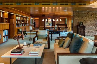 What Would Victor Do? - Photo 7 of 11 - Warmth permeates the living room,<br>where Honduran mahogany paneling,<br>bookshelves and built-ins stand<br>sumptuously in concert with birch<br>ceiling tiles, all caramelized with age.<br>Jeffrey P. Elliott executed the interior<br>design, weaving in the homeowners’<br>quirky collection of art, objects and<br>furnishings—no easy task considering<br>the Marianna von Allesch glass mural<br>juxtaposed with a toy monkey shaking<br>a martini. The striped chair in the<br>background is a rare Victor Hornbein<br>commission, one of a pair. The sculptural<br>staircase seems to float in place, belying<br>its satisfying weightiness underfoot.<br>A thin metal edge inserted into the<br>hardwood tread prevents slipping<br>and beautifully punctuates the Lou<br>and Romy Bieker design.