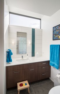 A light-enhancing transom window in the kids’ bathroom mimics the high-floating windows in the adjacent bedroom. Large-scale gray floor tiles and sleek cabinetry contrast with the playful vertical stripe in the tile ("the owners wanted a little bit of color and pop," says Goff); the hue mimics a teal blue seen throughout the home. Remove the children’s stool, and the bath will become sophisticated enough for a teen—or beyond. 