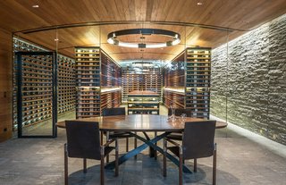 Naturally Modern - Photo 15 of 15 - SLOPESIDE CELLAR – A technical challenge from the get-go, this below-grade wine cellar is an addition to a 10,000-square-foot ski-in-ski-out residence. Just breaking ground meant a dig that extended well below the lowest footings of the existing home. The cellar’s design features only four materials (glass, mahogany, blackened steel, and Valser Quartzite cut three different ways), and is intended to make a clean departure from the stone-and-timber aesthetic of the home. The climate-controlled cellar, which has a capacity of 7,500 bottles, is seen behind glass panels that are recessed into both the floor and the undulated ceiling. An exterior glass wall provides views of a series of cascades that collect in a terminal pool at eye level. Photos by Audrey Hall.