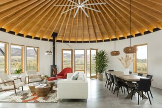 A Yurt-Inspired Vacation Home on the High Desert Plains of Colorado - Photo 2 of 8 - The largest of the three yurt structures houses the living and dining rooms and provides panoramic views. A geometric hide rug by Dedalo Rugs ties in pops of red from Eero Saarinen's Womb Chair, and pale blue from the Room and Board cushions on the sofa. The homeowners sourced the Oggetti Showtime coffee table from Wayfair. A pair of Kichler pendants define the dining area.