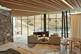 In this remote holiday rental home in New Zealand, guests can warm themselves by the asymmetrically-shaped fireplace while looking out to views of a gorgeous, deserted bay.