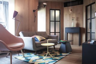 10 Small Apartments by a Hong Kong Design Studio That Are Less Than 1,000 Square Feet - Photo 5 of 10 - A colorful printed rug and matching cushion, a pink armchair, and plenty of bold geometric shapes give this apartment a slick, urban vibe.