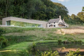 9 Traditional-Turned-Modern Cottages You Can Rent in the UK - Photo 2 of 9 - Sitting on a peaceful property within a 16-acre wooded valley near Cheltenham, The Find is a minimalist stone house with a new elongated extension that includes light concrete interiors and walls of glass windows. 