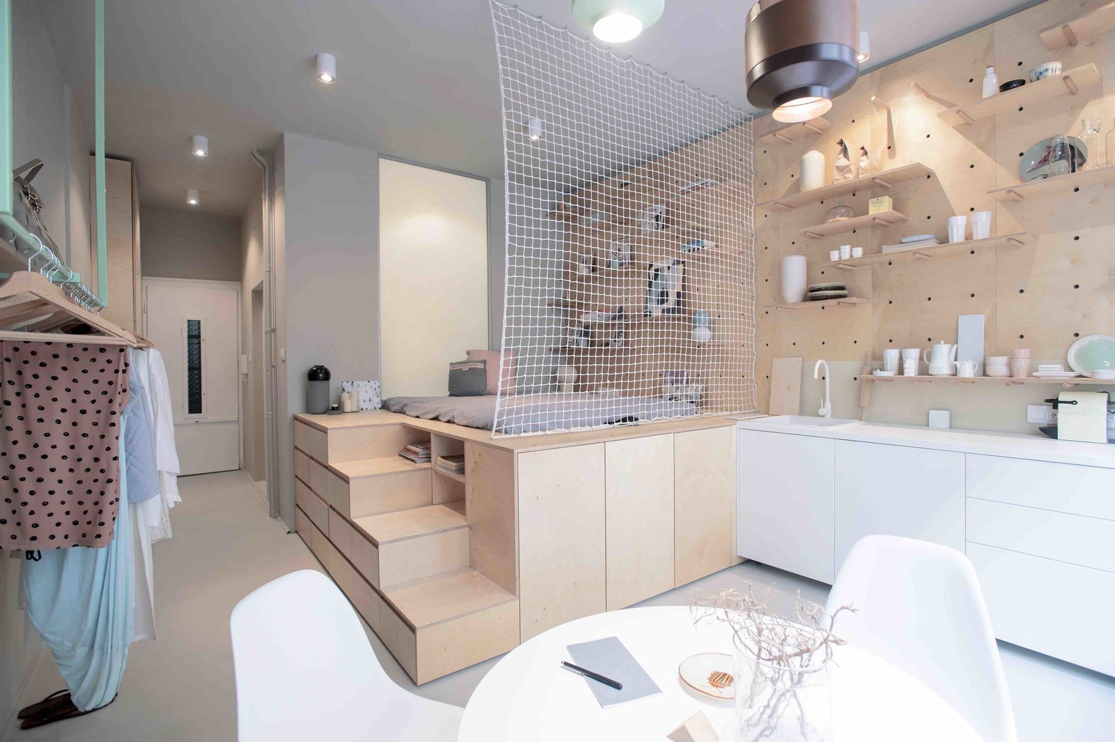To maximize space in this tiny 323-square-foot studio Budapest apartment, local design studio POSITION Collective used an elevated, plywood sleeping unit inspired by Japanese “tansu” mobile cabinetry, with secrete storage modules on the side of the steps leading up to the futon bed.