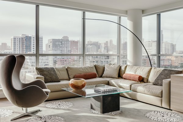 Modern home with living room, sofa, coffee tables, chair, floor lighting, sectional, and carpet floor. Madeline Weinrib custom wool and silk rug from Nepal, DWR corner sectional upholstered in Christian Liagre leather, custom wrap around bookcase in Italian wood laminate to match kitchen cabinetry. Egg Chair counterbalances longer arc of Yumi Floor Lamp. Coffee Table by All Modern and pillow fabric by Lee/ Jofa. Custom hand carved wood bowl by local artisan John Cobb from Urban Hardwood. Walls in Benjamin Moore Simply White OC-117. Photo of Arden Mission Bay Contemporary Condo