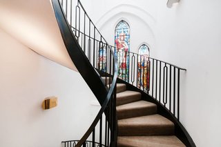 7 Repurposed Churches Around the World - Photo 1 of 8 - In the London neighborhood of Kenmont Gardens, a brick church's stained-glass windows provide a pop of color. It contrasts with the surrounding stark white walls and black powder-coated steel spiral staircase that connects the open-plan main level of the home to the bedrooms on the upper floors.