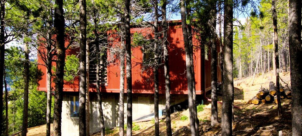 Siting closely within the surrounding pine forest, the Weehouse designed by Alchemy Architects and constructed by Irontown Homes rest only one half hour up the mountain from Boulder, CO.The tight driveway and secluded mountainside locale created an interesting delivery in which the modules were lifted by crane over the treetops and set into place. The pre-finished steel siding has been joined by a special fire protective shell due to lying in a high risk fire zone. The plethora of windows allow for natural sunlight to illuminate the warm, open interior.