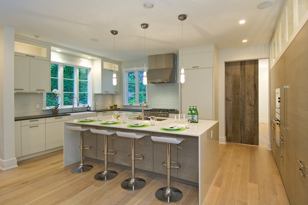 The open concept kitchen shares space with the Family room and views out to the covered porch. The cabinets are from Häcker and feature contrasting colors of white for the perimeter and a beach-wood finish on the island and pantry wall. The counters are ultra-compact material from Dekton with the permitter in a soapstone color with leather finish while the island features a dazzling smooth white color. The kitchen also features energy-efficient Miele appliances and a dedicated beverage fridge.
Special touches in this space include a full-size sink in the island to make meal prep and entertaining that much easier and a custom made barn door made from salvaged barn wood. The barn door serves as a generous passage to the dining room that can be easily closed for more formal occasions. Photo 6 of Greenwich Modern Barn modern home