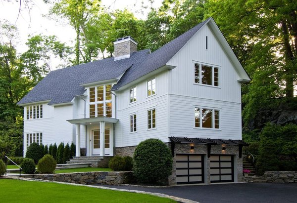 The modern barn style is defined by the vertical and horizontal siding patterns that emulate the feel of a classic New England Barn. The locally sourced stone is very natural and harkens to traditional stone foundations of the area.
Modern touches include sleek trim detailing, clean lines in the windows, frosted glass paneled garage doors and dark stained wood awning over the garage. Photo of Greenwich Modern Barn modern home