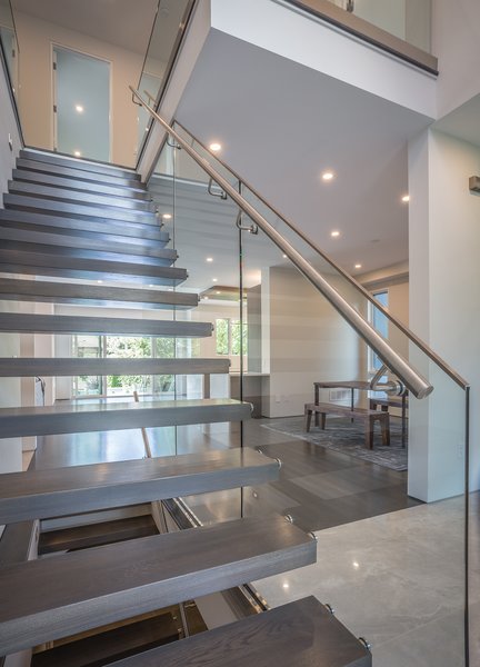 From the front, the open stairs allow site lines right to the large glazed areas at the far end of the house. From the entrance one sees the size of the space, divided with wall sections that delineate areas without blocking that view. Beyond is the large light source and view of the garden at the glazing, which in clement weather opens to enjoy breeze and space. Photo 5 of Shadow on White Pallet modern home