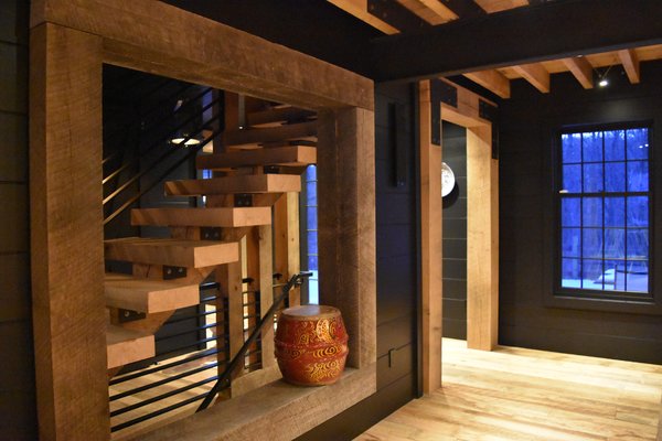Heavy oak timbers and rigid steel and oak stair case. Again, I like layering textures and color contrasts for dramatic effect. With exception to the red drum, the only color of this space is the oak itself. The floors and ceiling are oak including the large square opening. However the oak timbers used in the opening have been tanned in the sun for several months longer than the rest of the oak used throughout the home. Tanning oak will turn it gray. I chose to use the gray patina surface in this spot to provide a transition from the black walls to the lighter oak stairs. The gray seems to add dimension - leading you in towards the steps. Cultivating the oak patina using sunshine and careful rotation of the sides facing the sun, has allowed the lighter colored staircase to "pop" against the black background. Eventually, all of the oak in the home will silver and gray. It will take some time, but you can accelerate that process without "fuming" and "staining" by you use of water and sunshine. The process is highly labor intensive and requires great care. Wood will need to be wet and rotated several times daily and exposed to the sun. Rotation will reduce cupping of the wood. Oak (white, red, black oak) will all turn silver then various shades of dark gray. Pine, Fir, and Hemlock will all turn golden at first, then slowly into amber browns. Photo 16 of The Lodge modern home