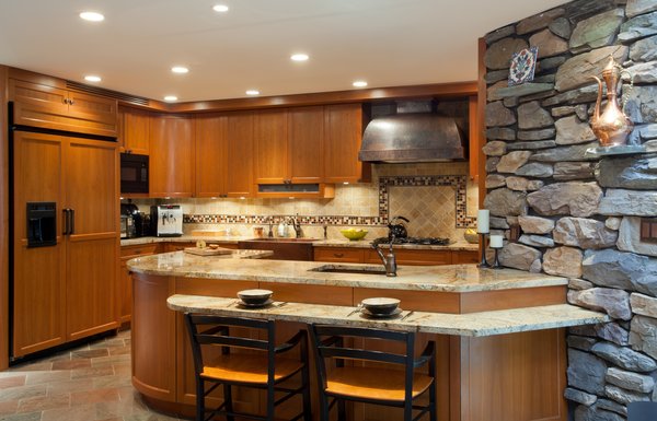 The cabinetry was custom designed and built out of cherry wood, and accented with oil rubbed bronze hardware. The counter tops are a rich golden sea granite, which is the same material used in the main dining room that connects to the kitchen where the bar is located.
A hammered copper vent over the range, as well as a hammered copper farm sink, added a rustic, handmade appeal to the kitchen. The backsplash is a mix of tumbled jerusalem gold stone, with a border throughout that pops up over the range area. The border is made up of 2 burnished metal pencil liner tiles, with a square, multi color glass mosaic in the center.
Photo 2 of Artisan Kitchen for a Nature Loving Family modern home