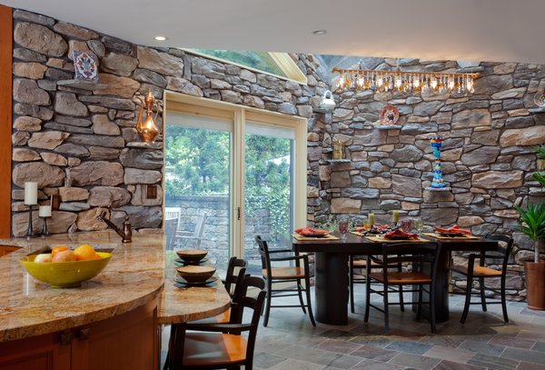 This private home is situated on a private street, right on the water, is surrounded by nature. It was important to this family, to bring in the elements of their outdoor patio and garden off the kitchen, into their interior. The stacked stone was the first element that was continued into the space, as well as the real slate flooring throughout the kitchen.
A custom chandelier was made to go over the eat in kitchen table. Custom built by Michael McHale, this industrial chic chandelier is made up of a mix of pipe and Swarovski crystals. It sits under a skylight above, and reflects colors and light over the table. Photo of Artisan Kitchen for a Nature Loving Family modern home
