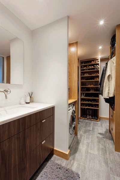The new wardrobe situation is impressive. A walk-in closet was already in place, but the couple had a better plan to build a more streamlined and highly organized pass-through closet. Using the door to the old closet, the GC custom built movable shelving units out of corresponding walnut wood for shoes. These movable units lead to a separate bathroom entry to the back of the studio, where the living room sits. The homeowners also gained a new compact washer/dryer to complete the turn-around. Photo 9 of Gramercy Studio Renovation modern home