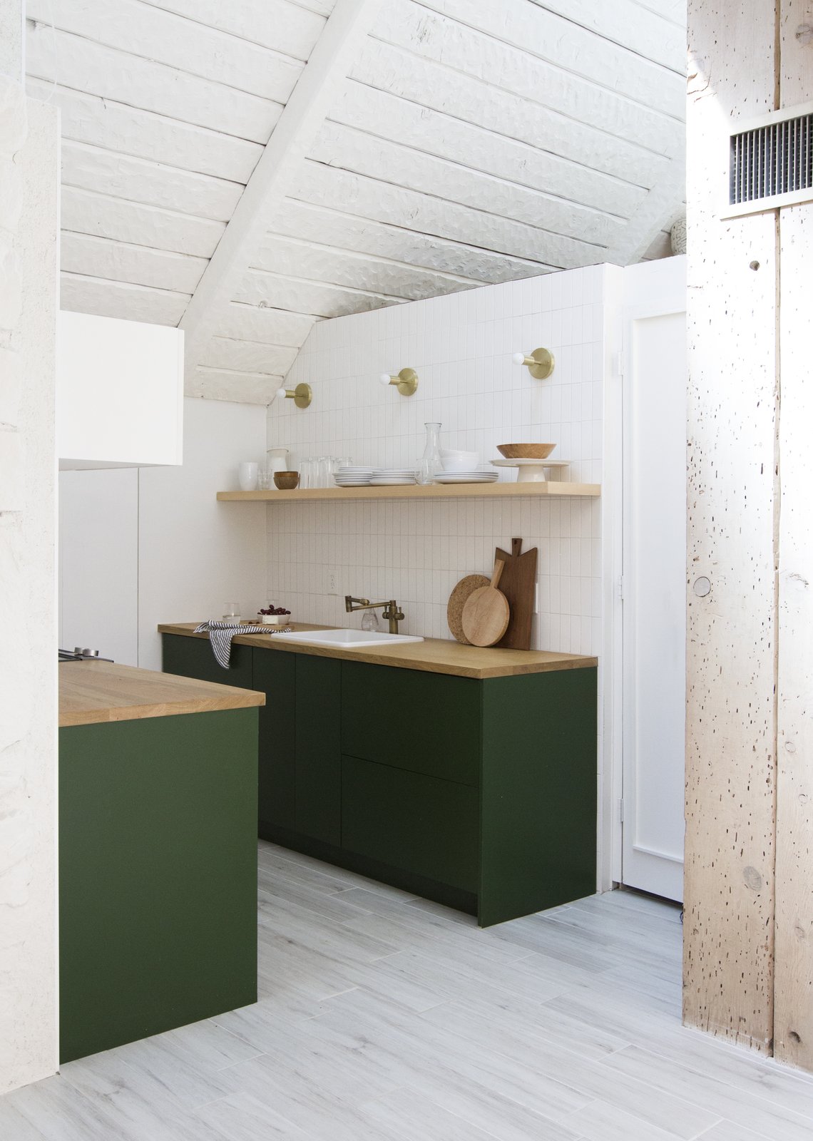 A view into the kitchen, which received IKEA cabinet boxes with Semihandmade drawer and door fronts painted Chard from Behr, by Samuel. The refrigerator is a KitchenAid model tucked under the butcher block counter and covered with a panel.