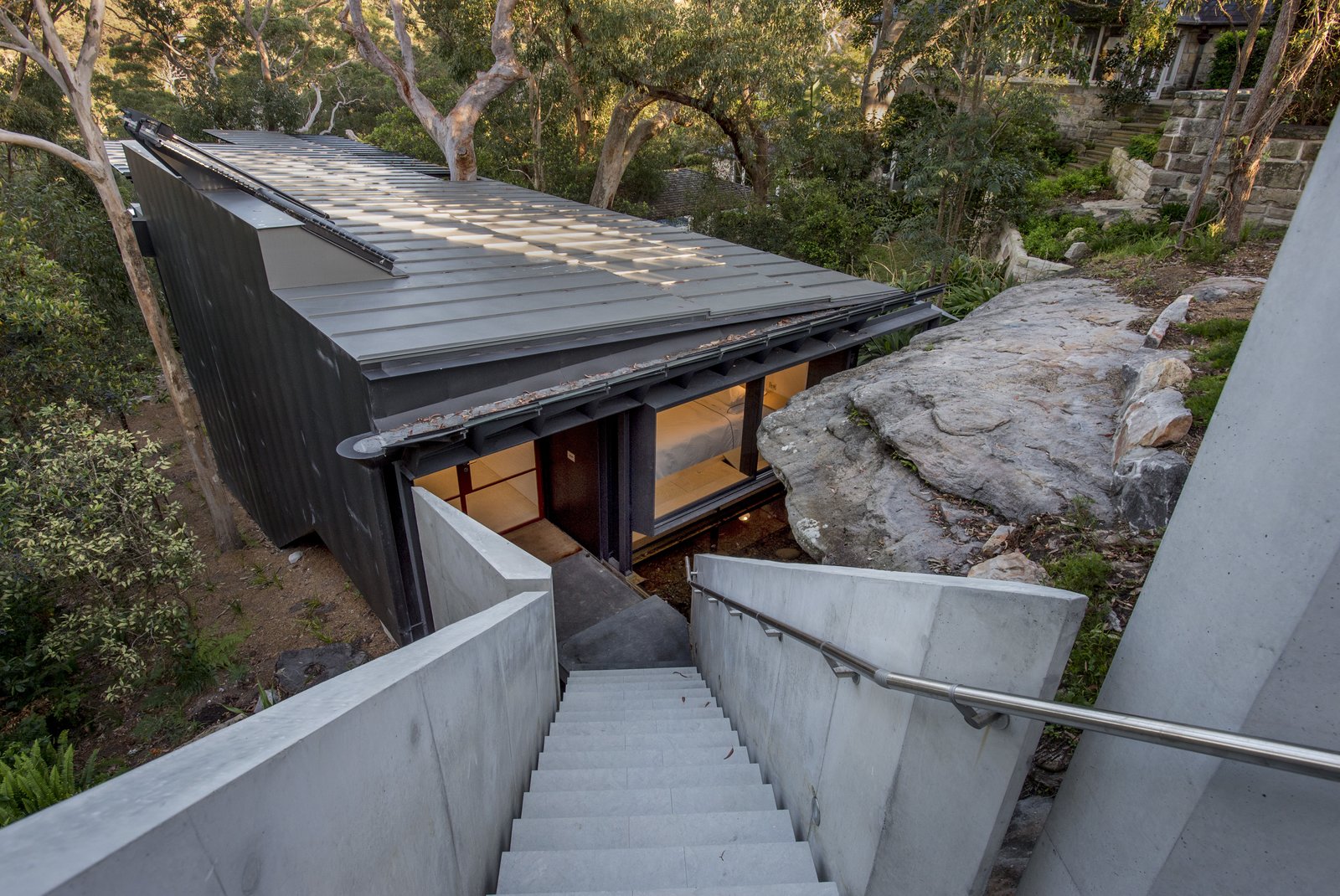 The house sits on a steep site and was positioned below a sandstone crop so as to be concealed from the street. The approach to the house is via a suspended concrete staircase.