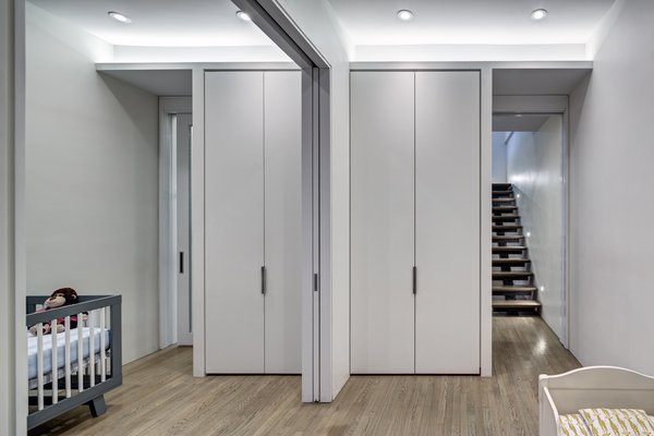 Modern home with interior, metal, sliding door type, bed, boy gender, toddler age, medium hardwood floor, bedroom, playroom, closet storage type, wood, and bedroom. Lower level: Children's Bedrooms
On the lower level, the use of pocketed sliding doors met an imperative client requirement. It allowed the children’s bed/playroom to be a flexible space - subdivided for sleep and open for play. Additional sliding glazed doors at the two entries to the bedrooms from the family room, facilitate deep penetration of natural indirect daylighting from the bedroom windows into the family area. Photo 13 of Noho Duplex, New York