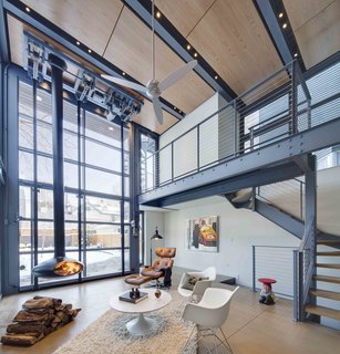 A Steel-and-Glass Addition With a Giant Hangar Door Maximizes Indoor/Outdoor Living - Photo 5 of 9 - The interior living space is warmed by the wood panels above and a hanging fireplace.