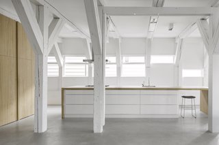 A Converted Warehouse in Amsterdam Boasts Soothing Interiors of Concrete and Wood - Photo 1 of 9 - The fully-integrated kitchen is obscured by oak cabinetry, corresponding with a large island with an integrated cooktop and sink. 