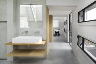 A Converted Warehouse in Amsterdam Boasts Soothing Interiors of Concrete and Wood - Photo 7 of 9 - A custom solid surface basin on oak wooden shelves, in combination with a Zuchetti faucet and a Vibia Linestra light fixture, make for a warm, contemporary bath vanity.