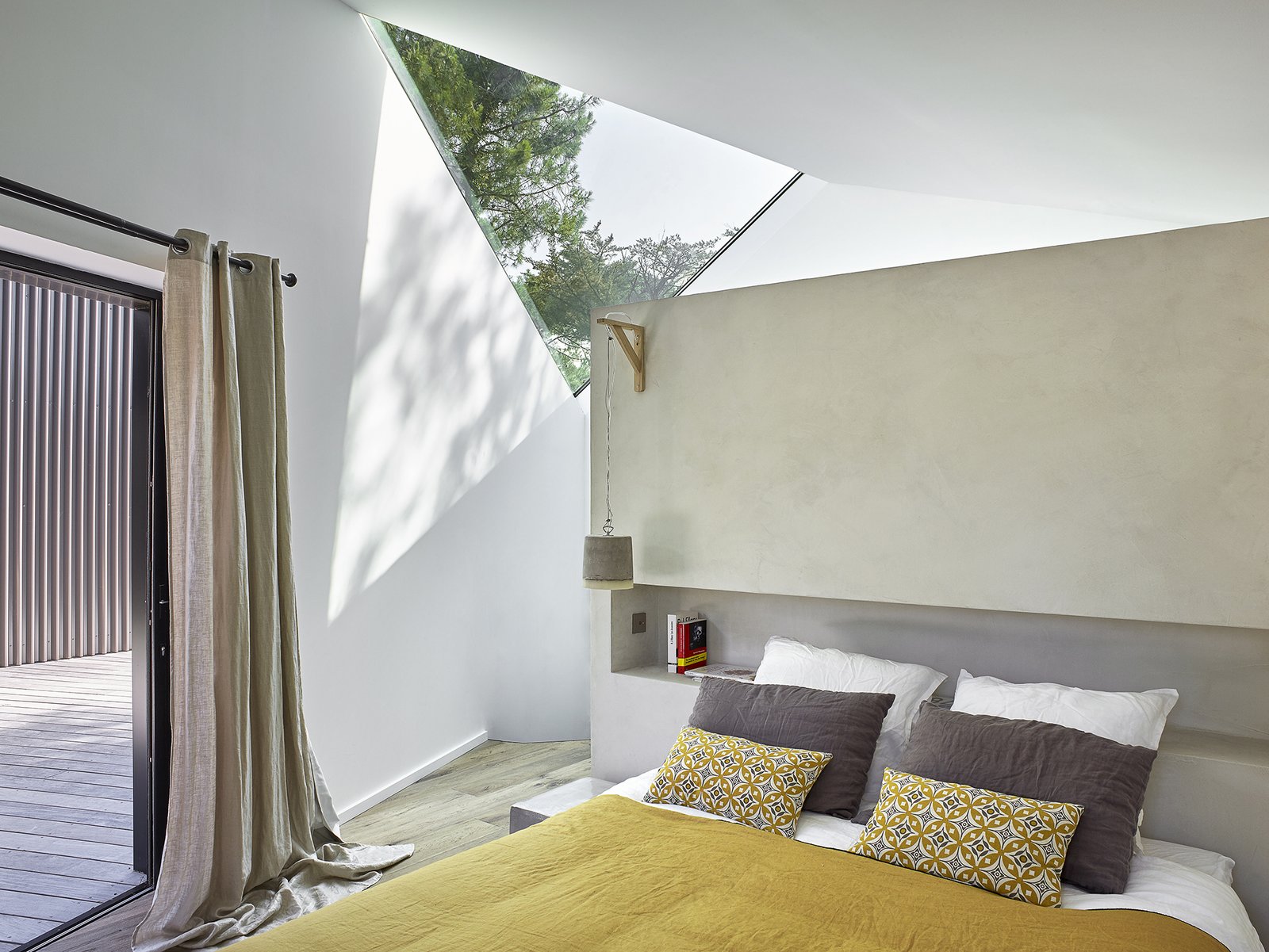 Triangular skylights make an appearance in the Master Bedroom as well. A concrete partition wall with a recessed bookshelf provides a custom headboard solution.