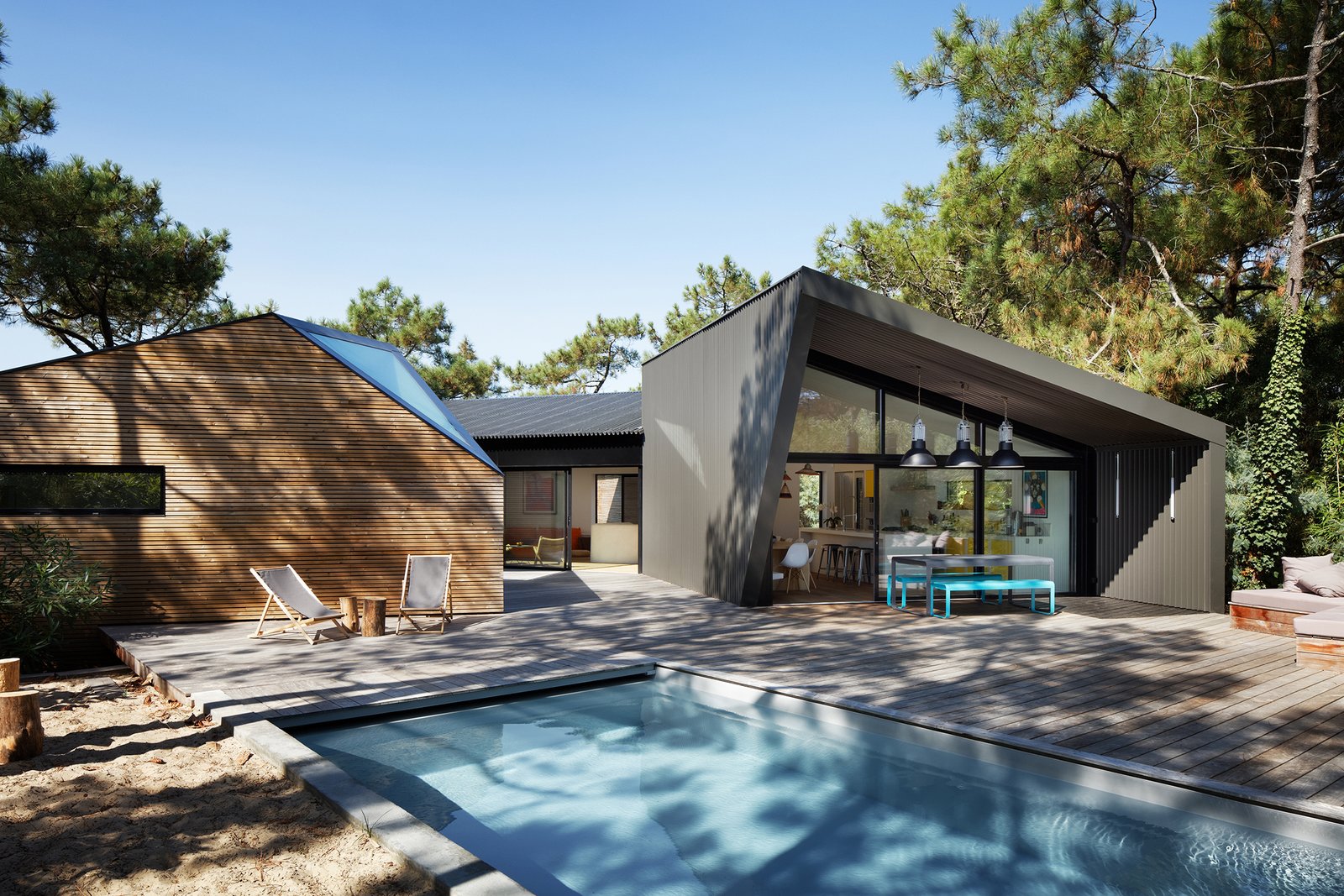 The wood wrapped exterior blends into the forest surround. Light and shadows of surrounding treas play on the textured facade.