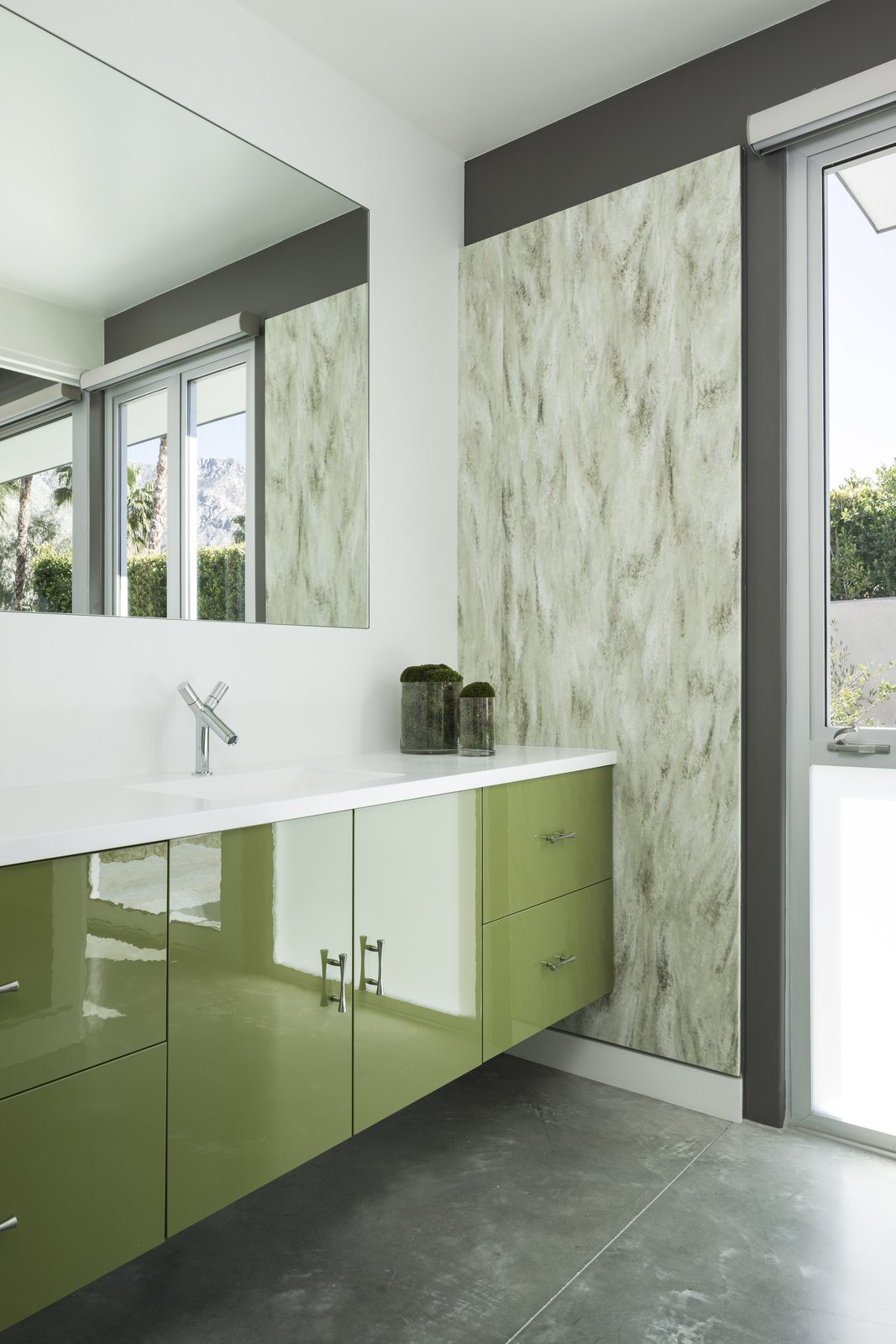 Glossy green cabinets, textured wall coverings, and polished concrete floors, in dessert hues, decorate one of the guest baths.