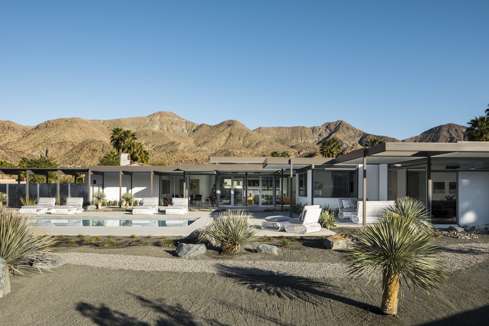 Mountainous terrain surrounds the modern, desert home. Horizontal roof planes extend outward, connected the home to the dessert land.