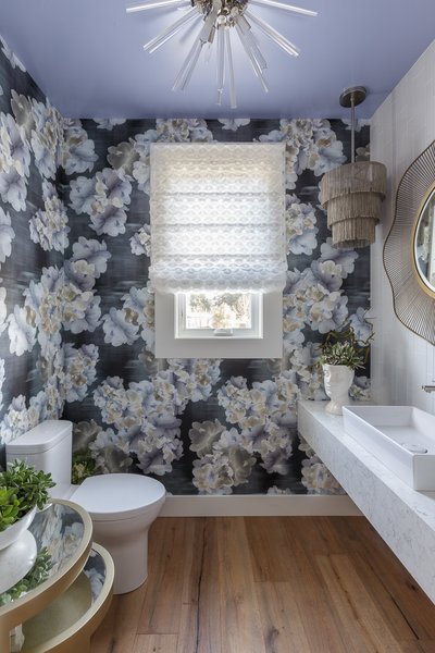 Modern home with bath room, medium hardwood floor, engineered quartz counter, pendant lighting, glass tile wall, vessel sink, and ceiling lighting. The Trove wallpaper offers a hint of that organic feel that is the Napa Valley but those flowers pop off the paper and offer just the right amount of bold pattern and color for a showhouse. The custom roman shade is made of a JAB Anstoetz fabric. The fabric was so delicate and reminded me of little petals and it compliments the wallpaper floral pattern nicely without competing with it and provides a soft texture next to the natural wood floor. The Arteriors Hanley glass flush mount light fixture added just a hint of glamour which I felt the floral wallpaper needed while still presenting an edge with the cut of the glass as opposed to being too feminine. Photo of Traditional Home Napa Valley Showhouse