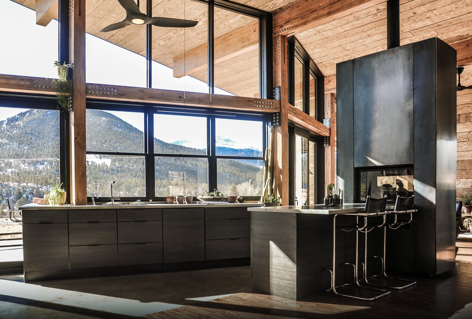 The warm industrial kitchen celebrates views of Rocky Mountain National Park beyond. A see-through, steel fireplace becomes a glowing beacon that warms the kitchen and living room at the heart of the home.